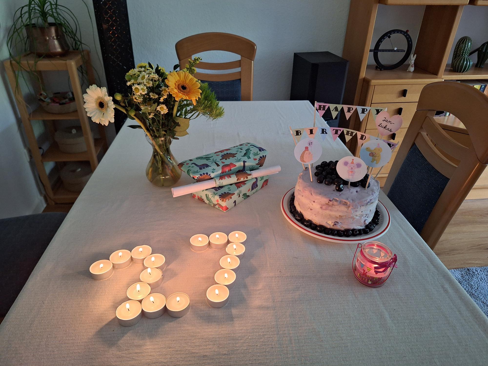 

AI generated caption: Candles spell "25" beside cake and flowers on table.