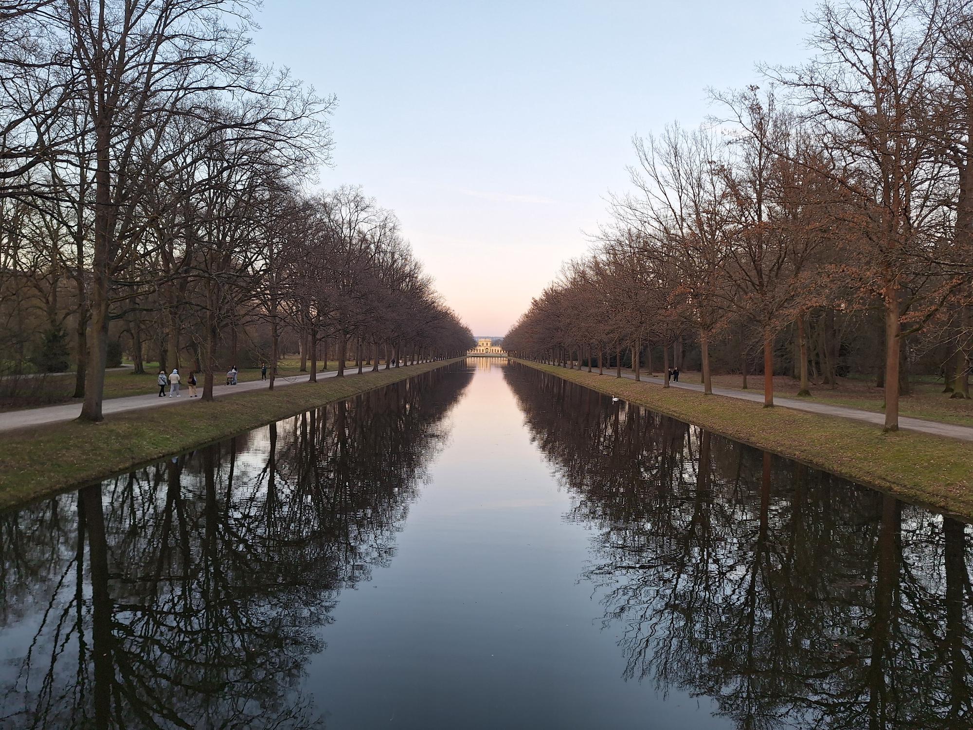 

AI generated caption: A long canal lined with bare trees reflects the sky.