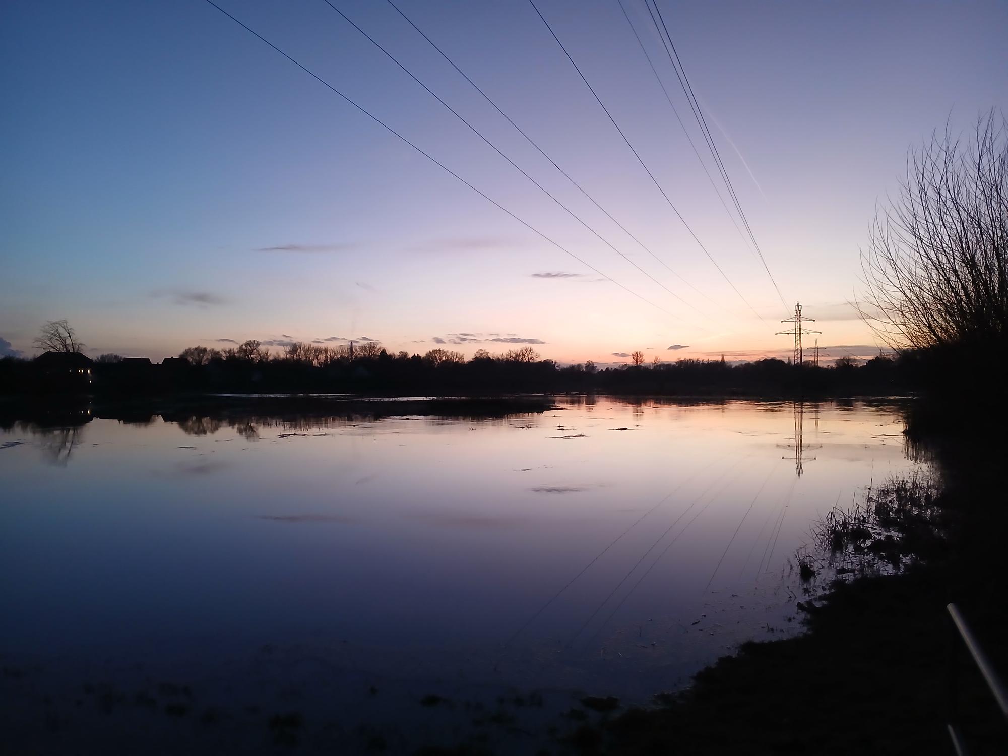 

AI generated caption: Power lines stretch over a calm lake during a purple and orange sunset.